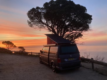 A campervan with a pop top roof parked overlooking a sunset after being taken to the best locations on the south coast of the UK.