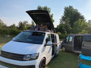 A campervan with children sat in the pop-top roof whilst keeping entertained on their family campervan holiday.