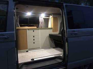 The interior of a campervan with custom lights and cupboards built in after the owner had a campervan conversion to level up its style