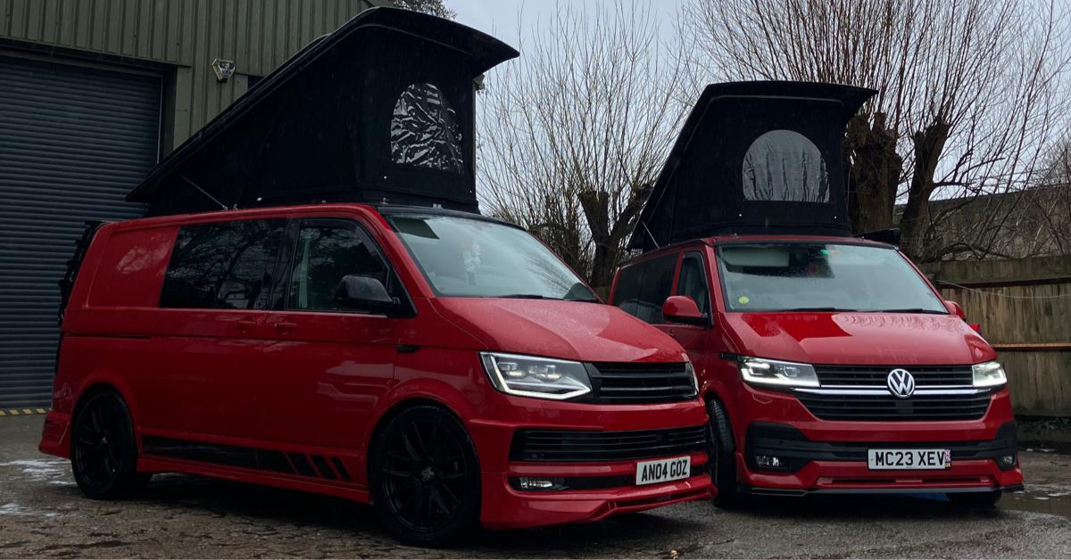 Two VW Transporter camper vans with their pop top roofs raised, showing the Stealth roof design on both vehicles outside the Van & Bus workshop.